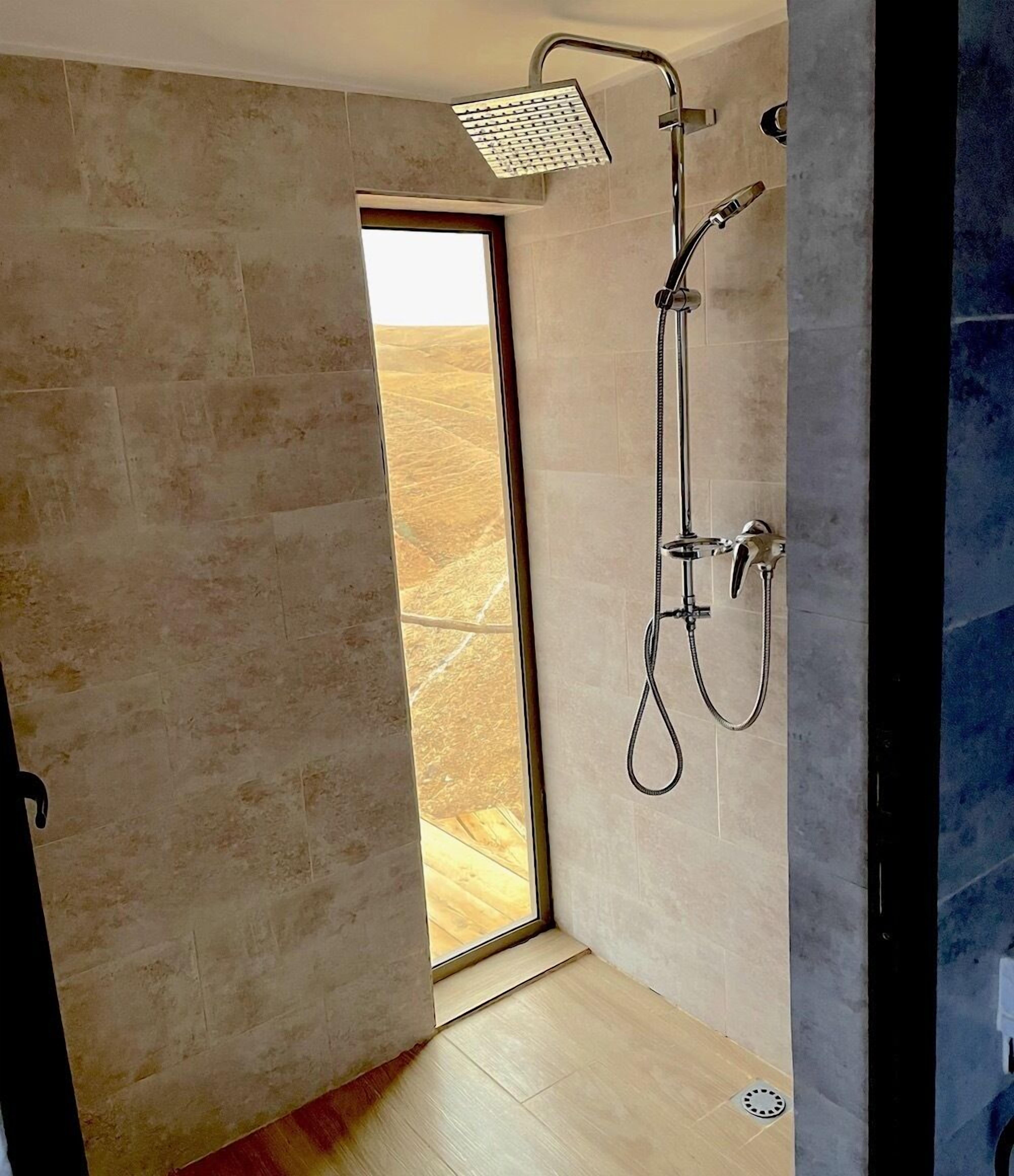 Un baño moderno con ducha, vista a través de un vidrio y suelo de madera.