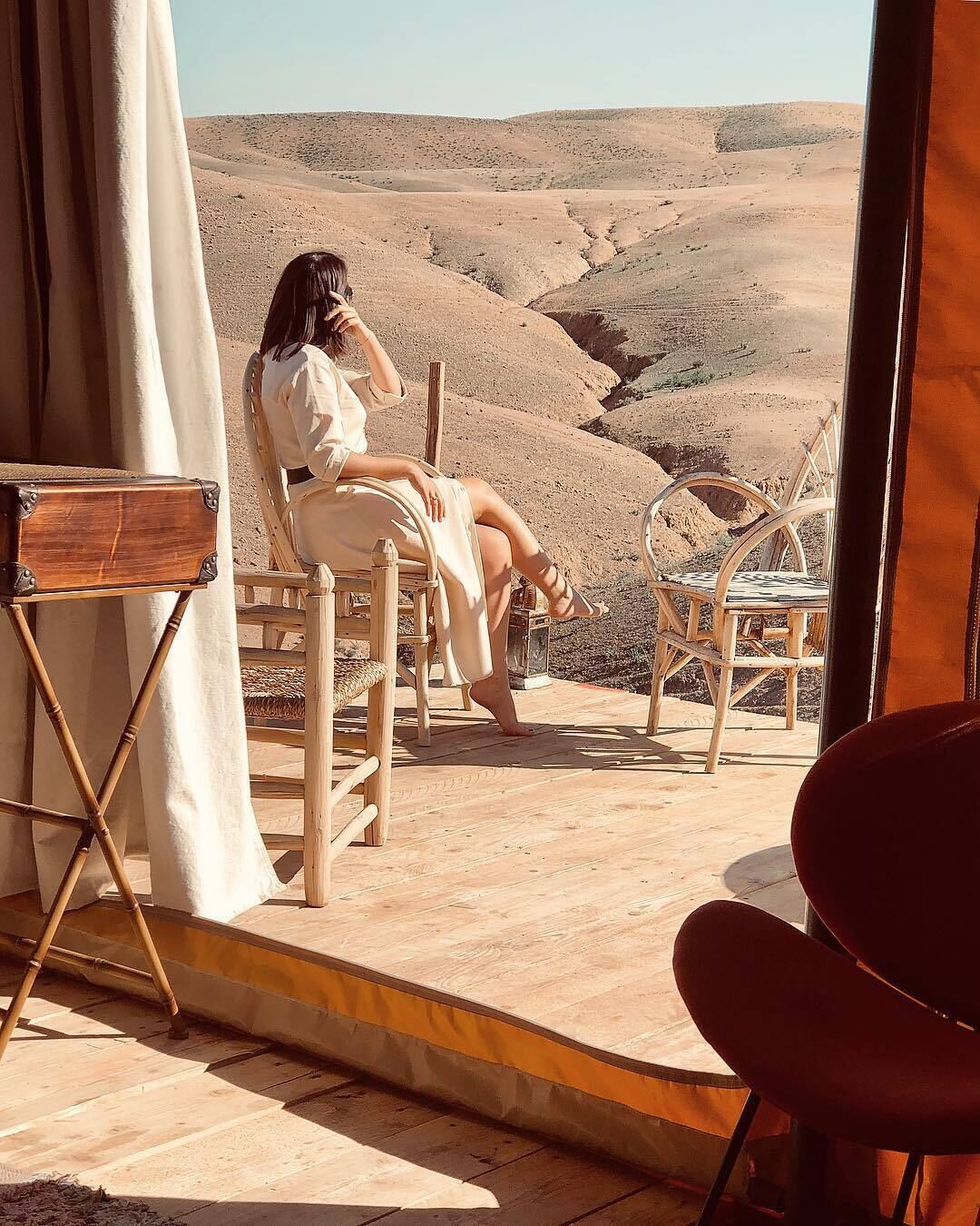 Ein Zimmer mit Blick auf eine Wüstenlandschaft, ein Holzstuhl, ein roter Sessel und ein kleiner Tisch.