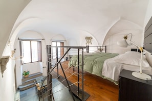 A bedroom with a bed, a desk, a chair, a staircase, and a window.