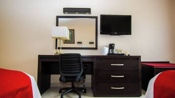 Habitación de hotel con escritorio, una silla, televisor, espejo y dos camas con ropa de cama roja y blanca.