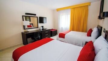 A hotel room with two beds, a desk, a chair, a TV, and a window with yellow curtains.