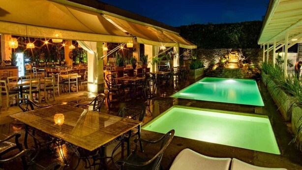An outdoor dining area with tables and chairs, a pool, and a bar area with umbrellas.