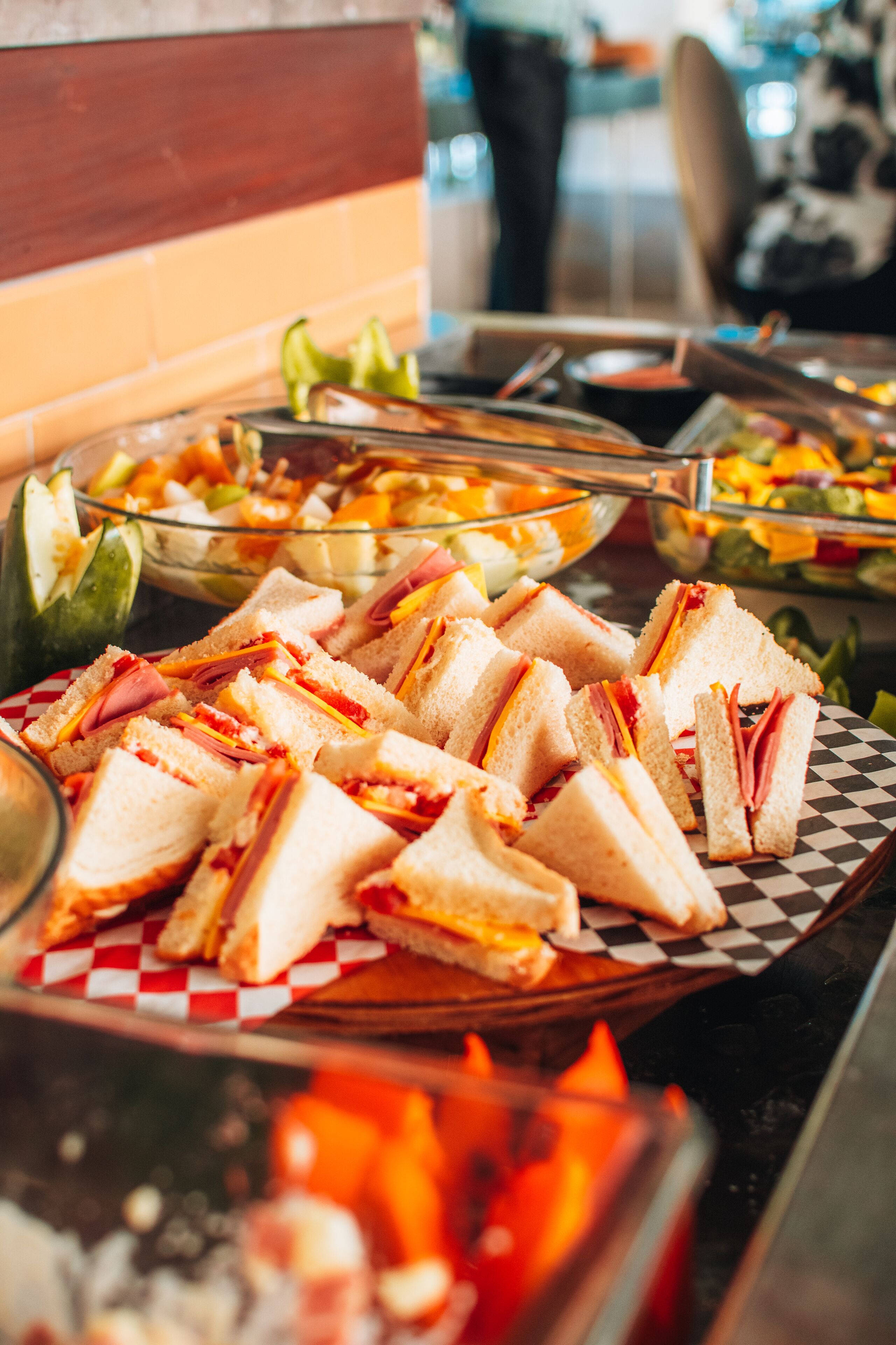 Mesa de buffet com sanduíches, saladas e uma cesta de frutas.