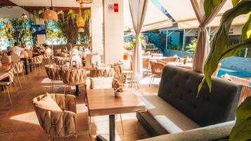 Un comedor interior con mesas, sillas, un sofá y plantas colgantes.
