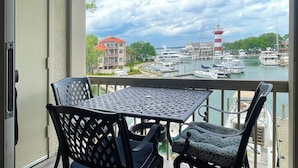 A balcony with a table and chairs overlooking a marina with boats and a lighthouse. - 1034 Caravel Court at The Sea Pines Resort (Hilton Head Island)