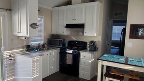 A compact kitchen with white cabinets, a microwave, stove, and a small dining area with a table and chairs.