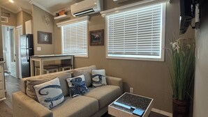 A living room with a beige sofa, a coffee table, and a kitchen in the background.