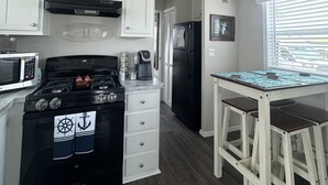A kitchen with white cabinets, a black stove, a refrigerator, and a dining table with bar stools.