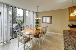 A dining area with a wooden table and white chairs, a ceiling light, and a view through large glass doors. - 1252 Harbour Town Club at The Sea Pines Resort (Hilton Head Island)