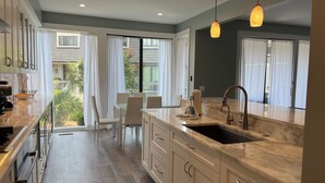 A modern kitchen with a marble countertop, a sink, and a dining area with chairs. - 1259 Harbour Town Club at The Sea Pines Resort (Hilton Head Island)