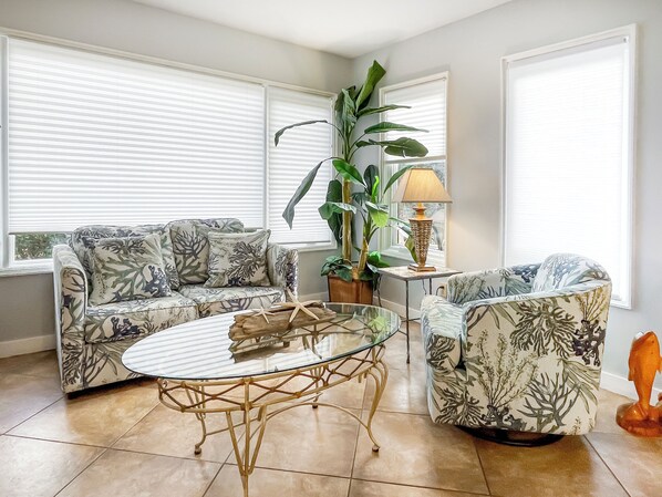 A living room with a sofa, armchair, glass coffee table, and a lamp. - 1404 South Beach Villa at The Sea Pines Resort (Hilton Head Island)