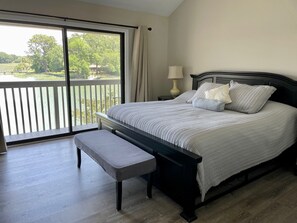 A bedroom with a large window, a bed, a bench, and a nightstand with a lamp. - 1617 Port Villa at The Sea Pines Resort (Hilton Head Island)