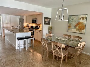 A modern kitchen with white cabinets, stainless steel appliances, and a glass dining table with wooden chairs. - 1617 Port Villa at The Sea Pines Resort (Hilton Head Island)