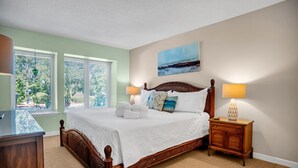 Une chambre à coucher bien aménagée, avec un grand lit, deux tables de chevet et une vue sur l’extérieur par les fenêtres.