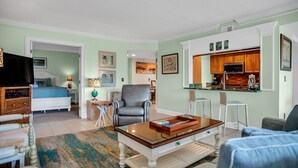Un salon bien éclairé, équipé d’une télévision, d’un canapé confortable, d’une table basse et d’un coin cuisine avec des meubles en bois et un four à micro-ondes.