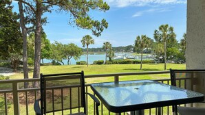 A balcony with a glass table and chairs, overlooking a lake with boats and palm trees. - 1805 Bluff Villa at Sea Pines Resort (Hilton Head Island)