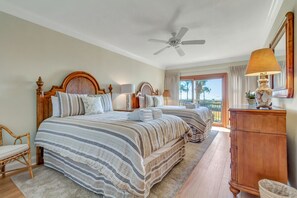 Habitación de hotel con dos camas, ventilador de techo, cómoda de madera y vista al exterior.
