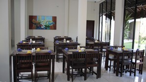 A dining area with multiple tables and chairs, a large painting on the wall, and large windows allowing natural light. - Pousada Vila do Porto (Ipojuca)