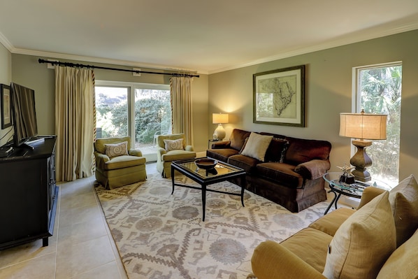 A living room with a sofa, armchairs, a coffee table, a TV, and a lamp.