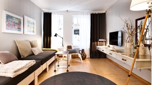 En moderne stue med sofa, skrivebord, fjernsyn og billedkunst på væggen.