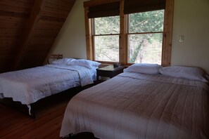 Quarto com duas camas, vigas de madeira no teto e uma janela grande com vista para árvores.