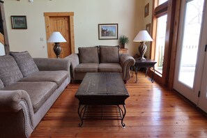 Uma sala de estar com piso de madeira, dois sofás, uma mesa de centro e duas luminárias.