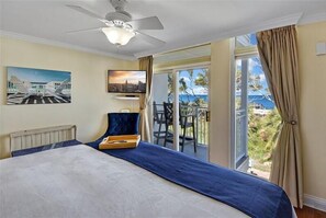 Ett hotellrum med en säng, en takfläkt, en TV och en balkong med utsikt över havet.
