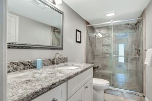 A bathroom with a granite countertop, a sink, a toilet, a glass-enclosed shower, and a large mirror. - 2236 Heritage at The Sea Pines Resort (Hilton Head Island)