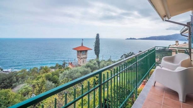 Un balcón con vistas al mar, una torre y follaje.