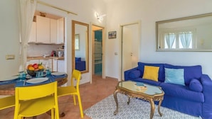 Una sala de estar con un sofá azul, un sillón amarillo y una mesa de centro de vidrio.