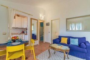 Una sala de estar con un sofá azul, un sillón amarillo y una mesa de centro de vidrio.