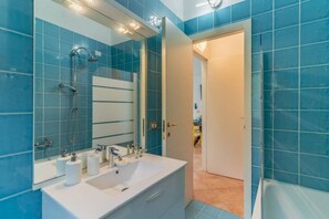 Un bagno con piastrelle blu, un lavandino bianco, uno specchio e una doccia.