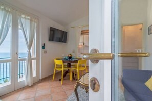 Una stanza con zona pranzo, televisione a parete e vista sul mare attraverso ampie finestre.