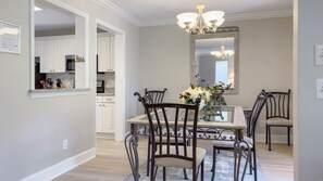 Een eetruimte met een tafel met glazen blad, omringd door vier stoelen, een kroonluchter en een spiegel boven de tafel.