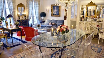 A spacious living room with a glass-top dining table, red armchairs, a blue sofa, and a chandelier.