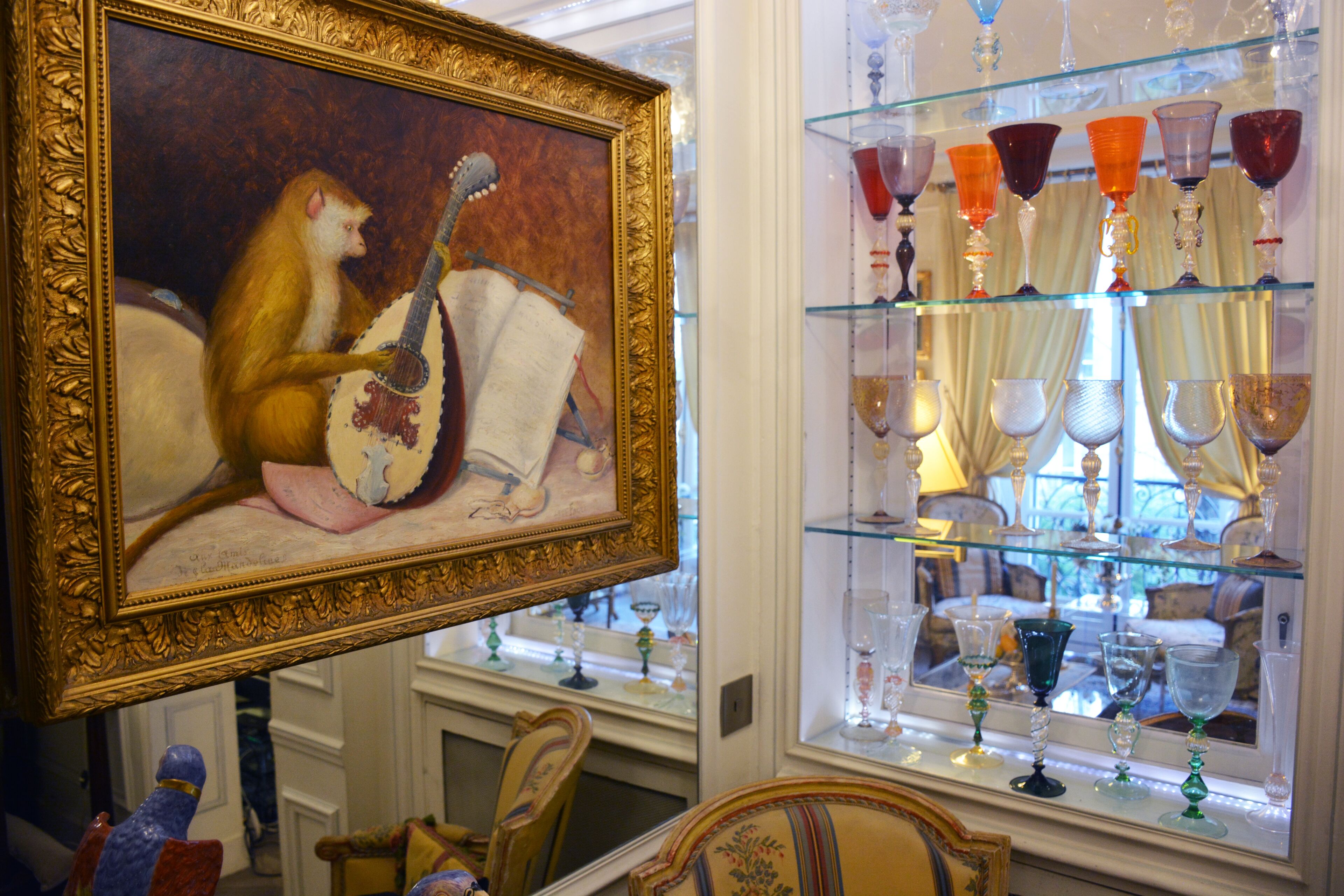 A room with a framed painting, a glass display case with various glassware, and a mirror reflecting part of the room.