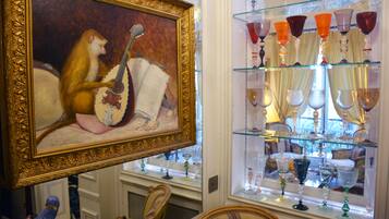A room with a framed painting, a glass display case with various glassware, and a mirror reflecting part of the room.