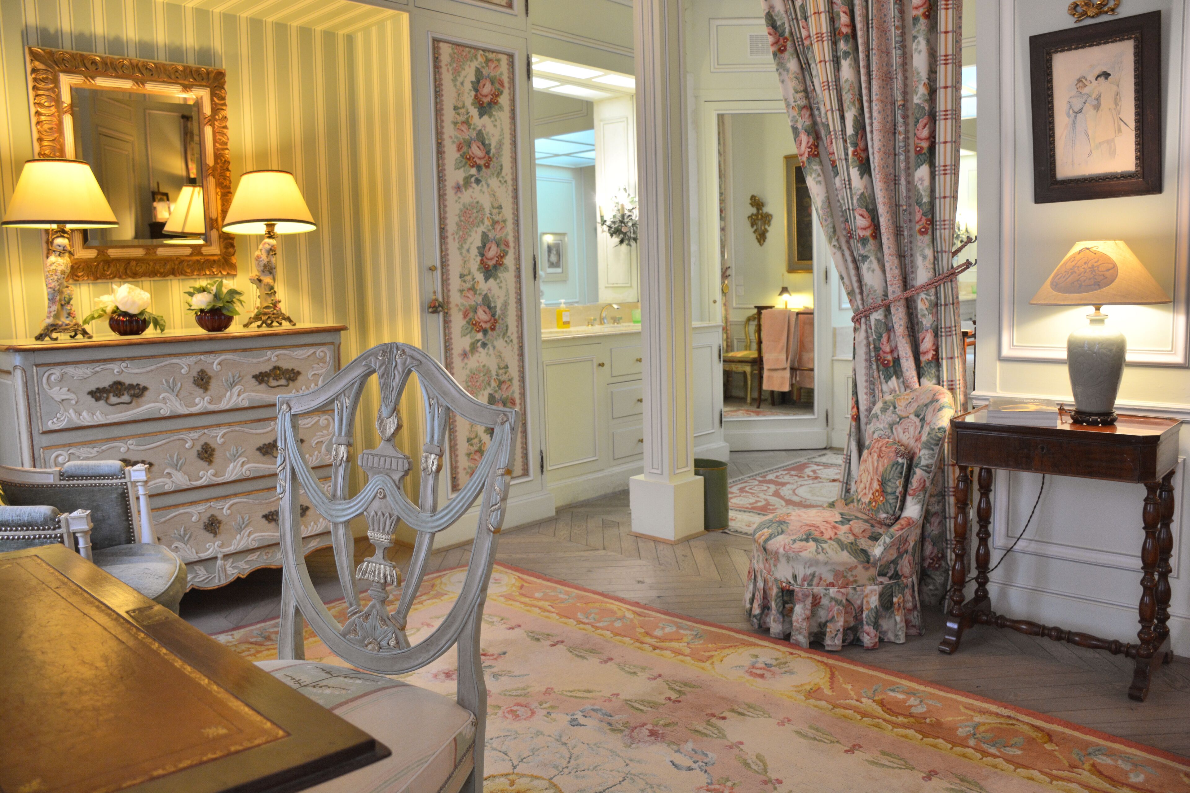 A room with a large mirror, a floral chair, a table with a lamp, and a floral-patterned curtain.