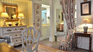 A room with a large mirror, a floral chair, a table with a lamp, and a floral-patterned curtain.