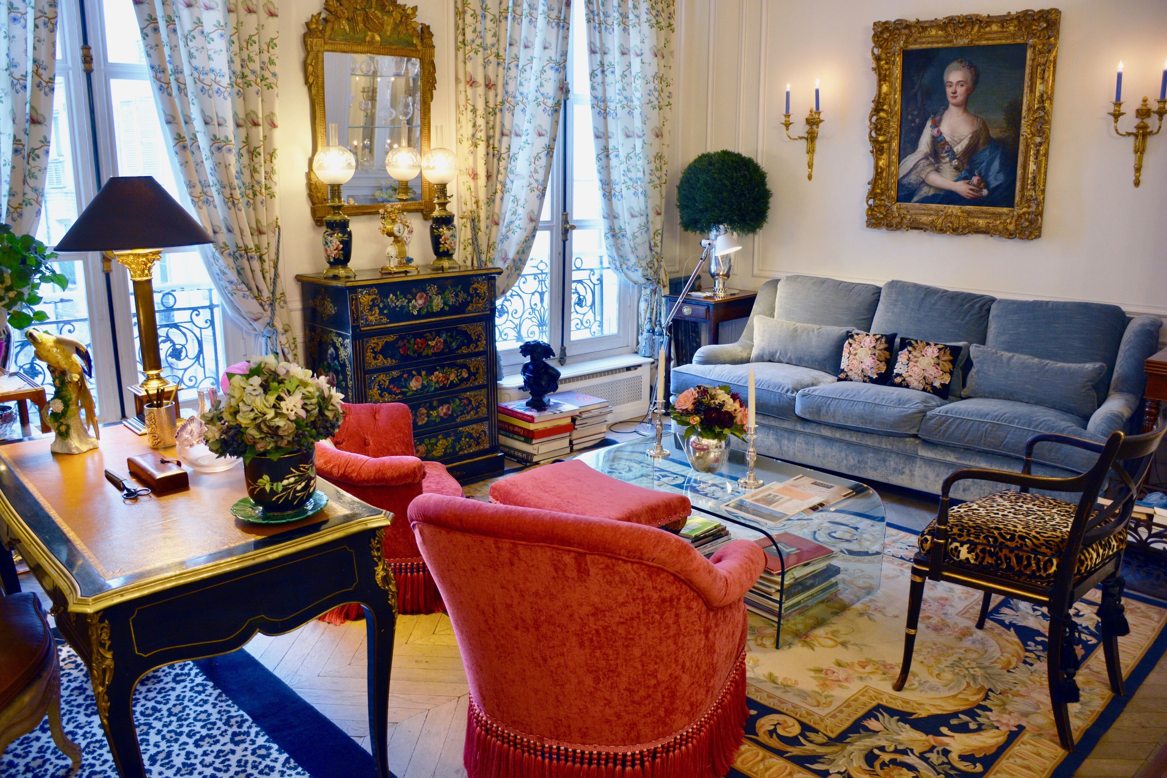 Une pièce avec un canapé bleu, un fauteuil rouge, une table en bois avec une lampe et un miroir décoratif.