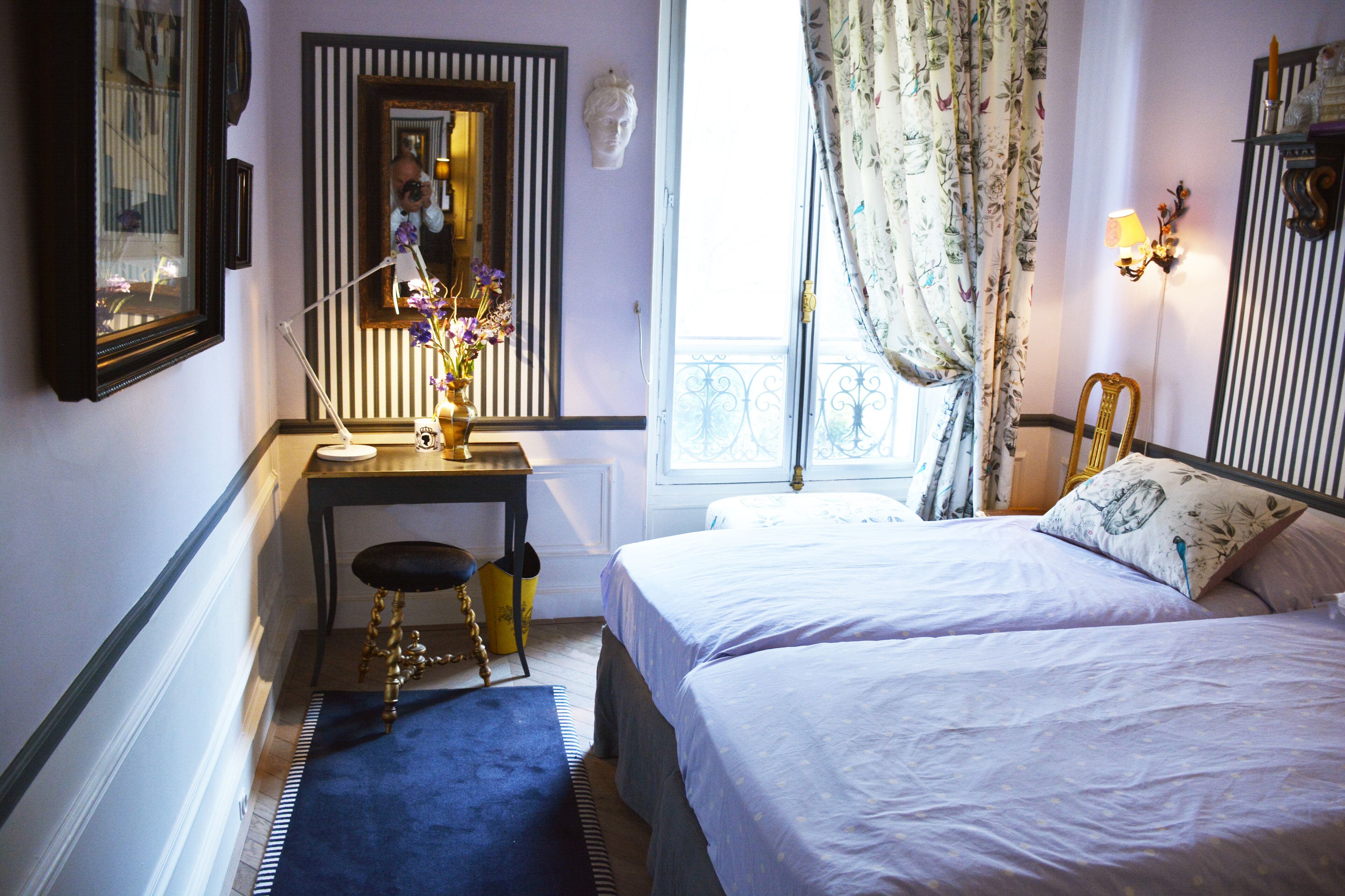 A bedroom with two beds, a desk with a chair, a mirror, and a window with curtains.