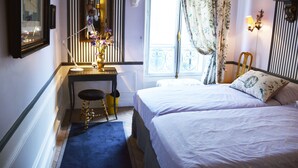 A bedroom with two beds, a desk with a chair, a mirror, and a window with curtains.