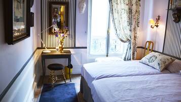 A bedroom with two beds, a desk with a chair, a mirror, and a window with curtains.