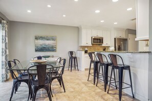 A modern kitchen with white cabinets, a granite countertop, and a dining area with a glass table and metal chairs. - 2302 Heritage Villas at The Sea Pines Resort (Hilton Head Island)