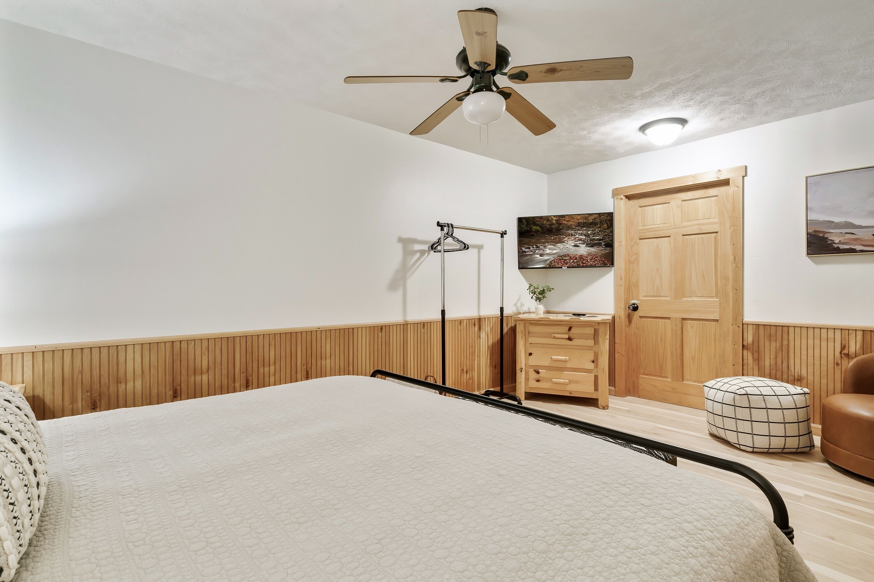 Un dormitorio con cama, armario de madera, una puerta, lámpara colgante y ventilador de techo.