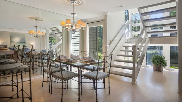 Une salle à manger spacieuse avec un haut plafond, un lustre moderne et un escalier menant à un niveau supérieur.