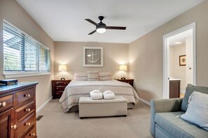 Une chambre à coucher comprenant un lit, deux tables de chevet avec des lampes, un ventilateur de plafond, une commode et une fenêtre avec des stores.