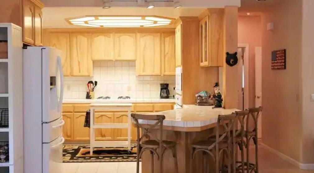 Een keuken met houten kastjes, een witte koelkast, een koffiezetapparaat en een eethoek met stoelen.