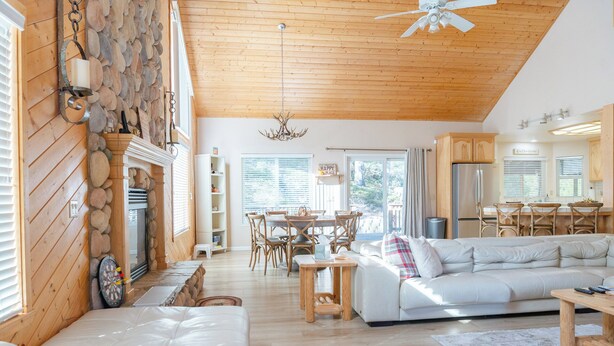 A spacious living area with a fireplace, wooden ceiling, and a dining area with a view of the outdoors. - Spacious cabin with game room free WIFI & parking (Shaver Lake)
