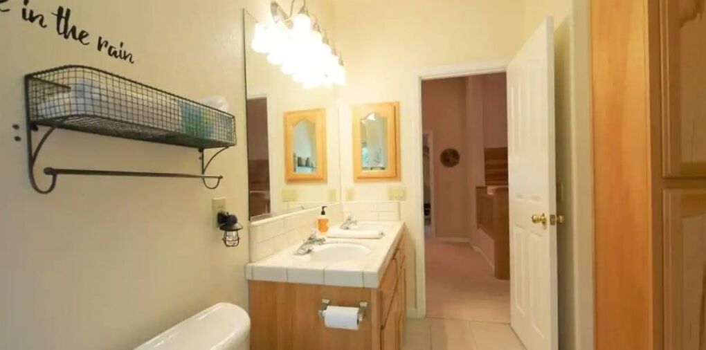 A bathroom with a double sink, a mirror, a towel rack, and a toilet.